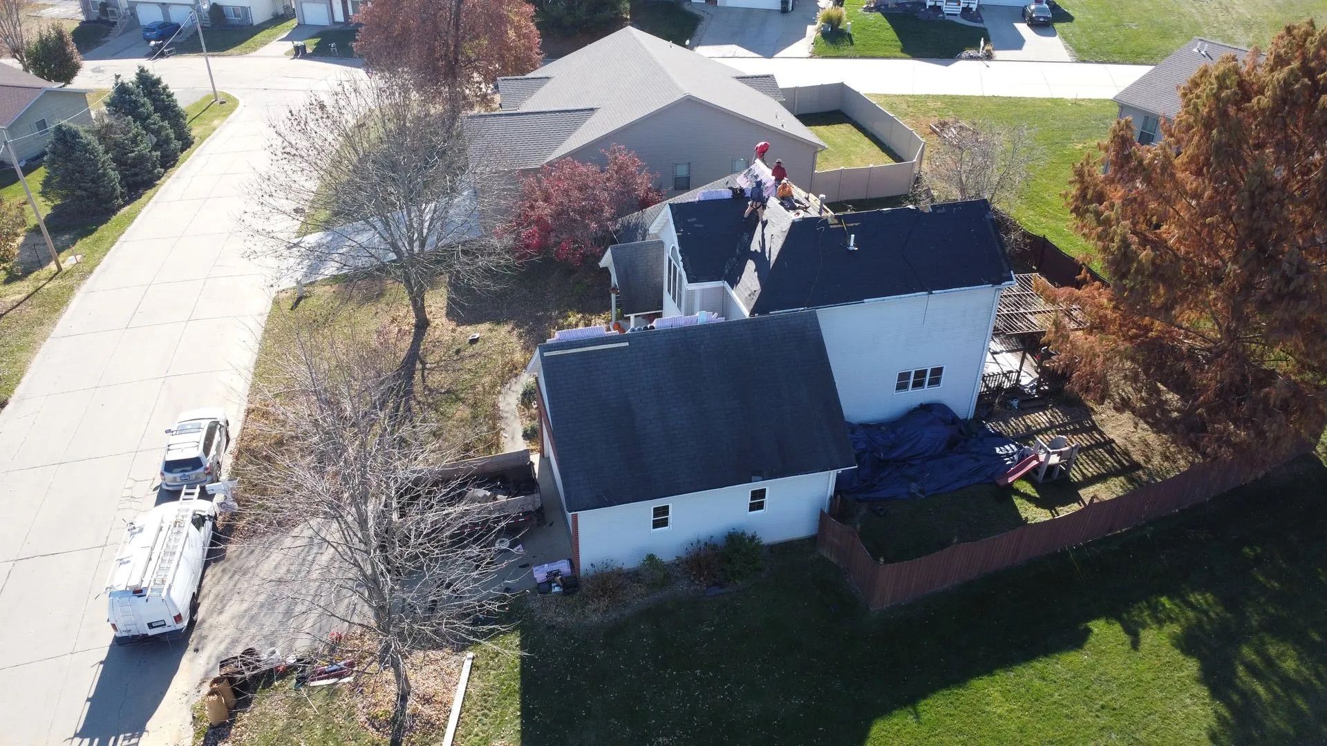 Aerial view of a house with workers on the roof. A white truck is parked nearby.