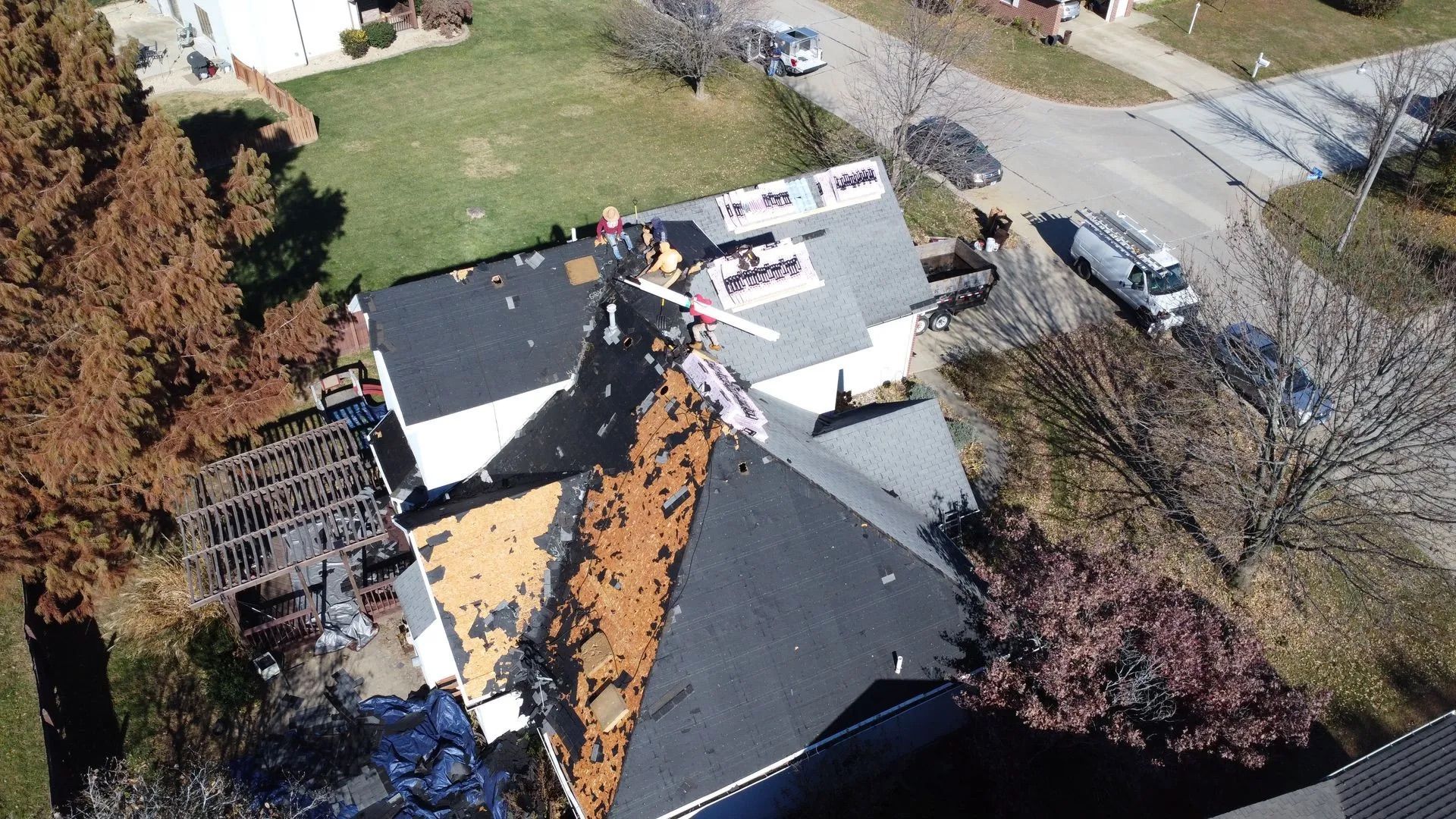 Aerial view of a house roof partially covered with new shingles while workers are on the roof.