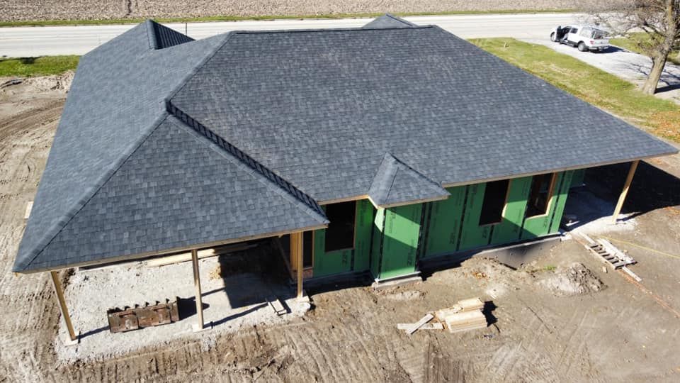 New house under construction with a dark gray shingled roof, green siding, and exposed wooden beams.
