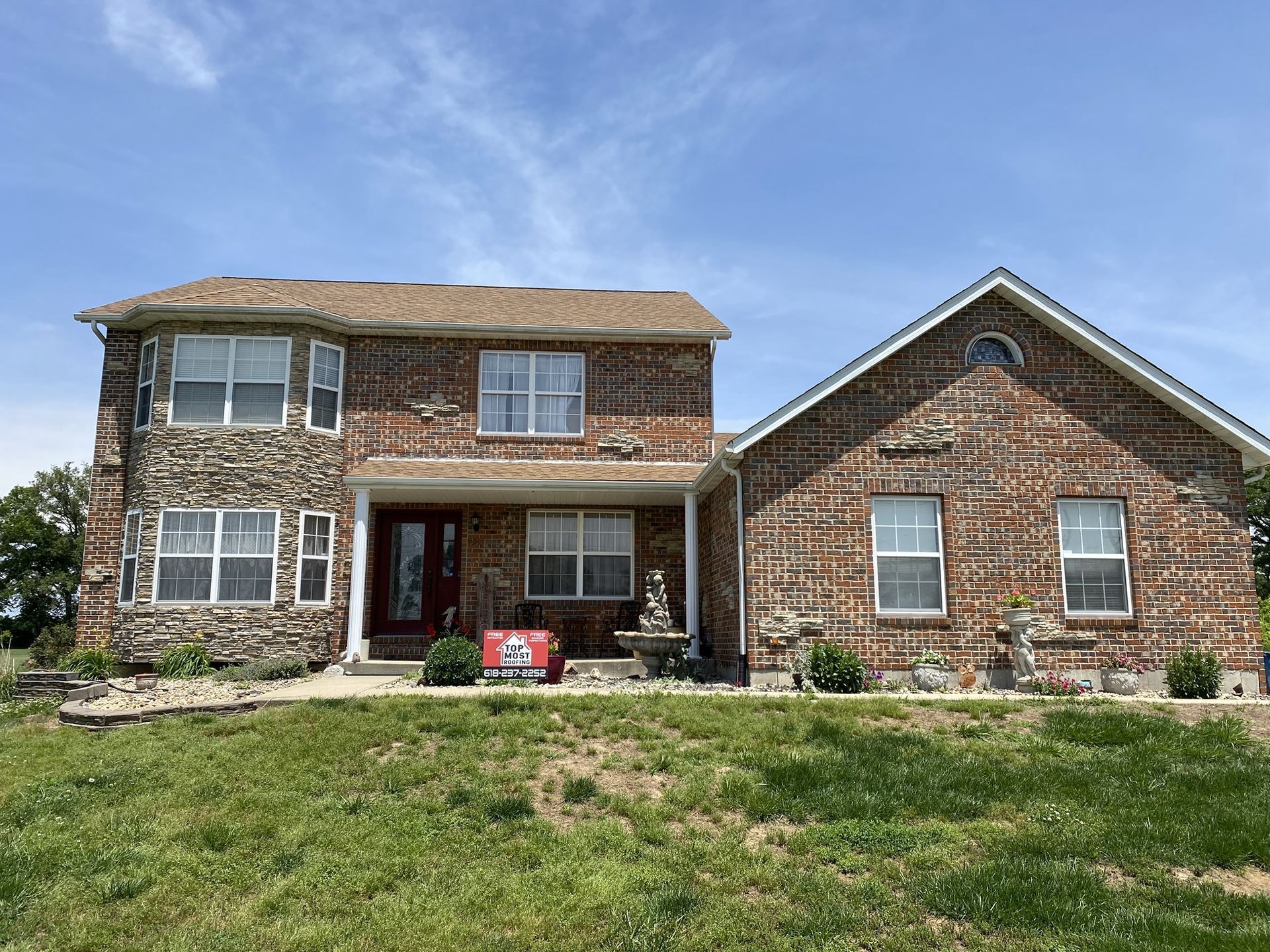 Two-story house with brick and stone exterior, light blue sky, and green grass lawn.