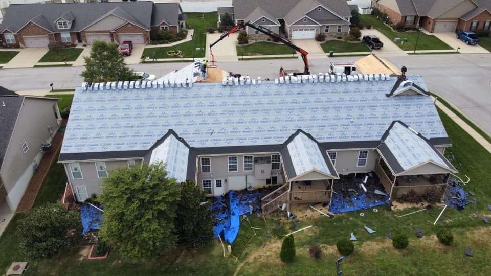 Roofing work in progress on a two-story house with blue tarps on the ground. A crane is visible.