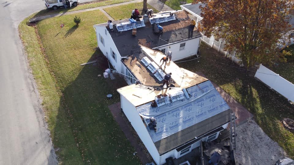 Roofers working on a residential house, replacing shingles. Brown roof, green grass, overcast day.