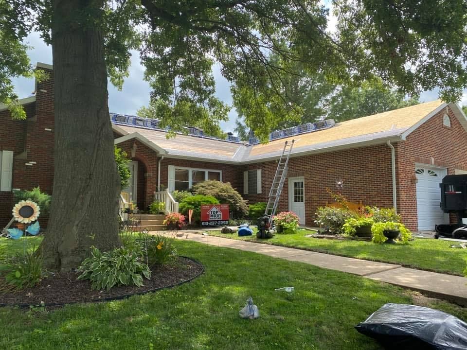 House with roof partially replaced; ladder, tools, and materials are visible on the roof and lawn.