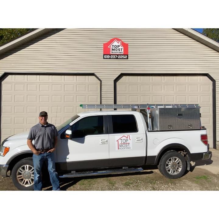 Man standing beside a white truck with a roofing logo in front of a garage.