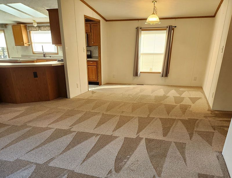 A kitchen and dining room with a wooden counter, beige patterned carpet, a single window with curtains, and a light fixture.