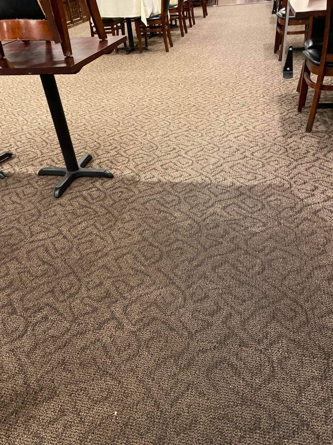 A restaurant interior featuring tables and chairs arranged on a two-toned, patterned carpeted floor.