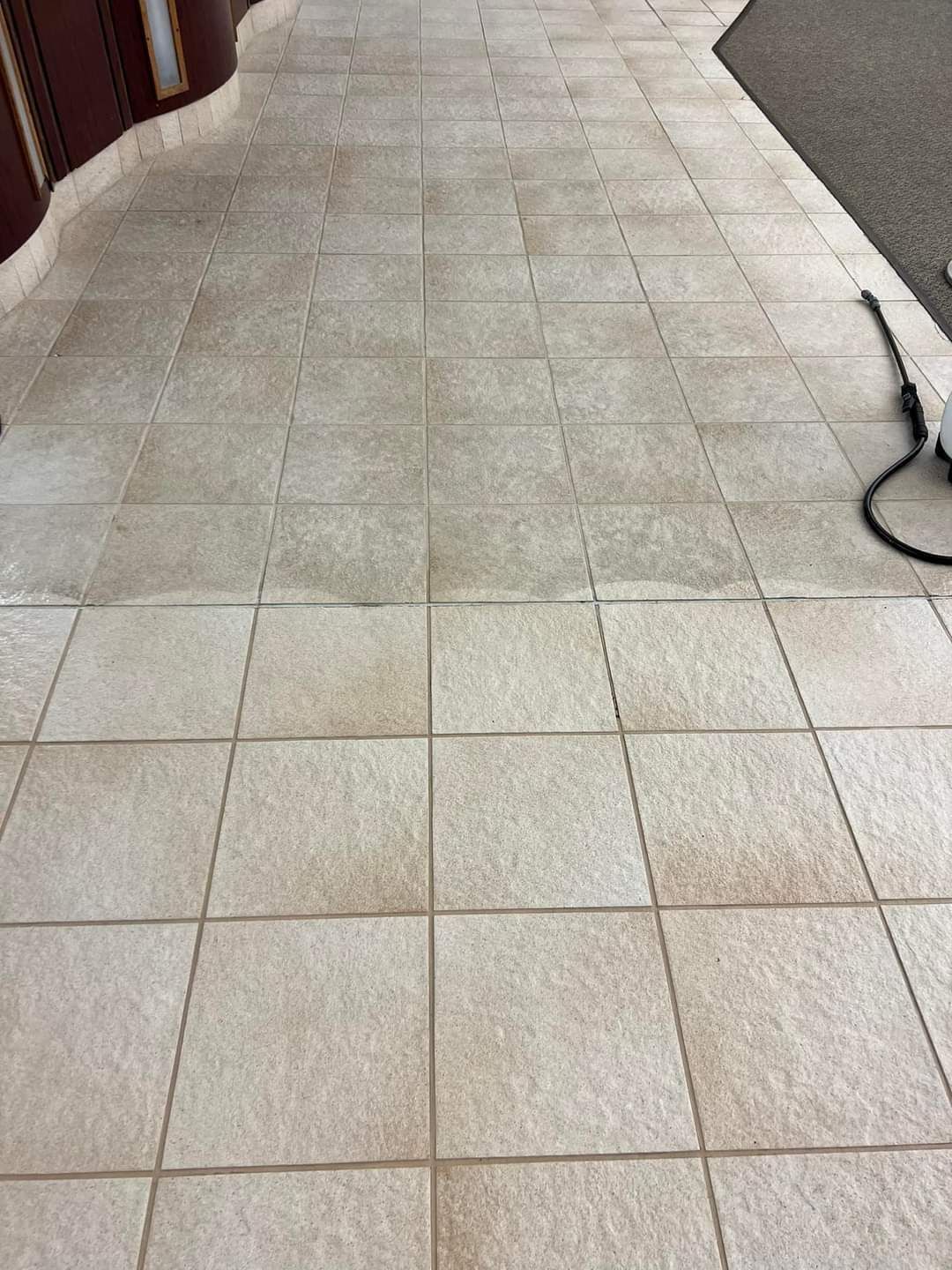 A power washer cleaning a stone patio, showing a clear contrast between the dark, soiled surface and the clean, light tile.