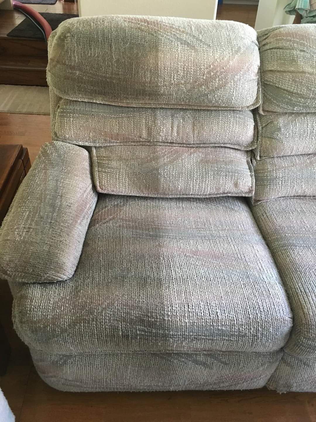 A close-up view of a textured, light gray fabric recliner sofa on a wooden floor.