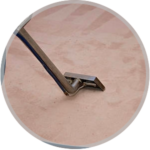 A close-up view of a metal carpet cleaning wand tool being used on a light-colored carpet.