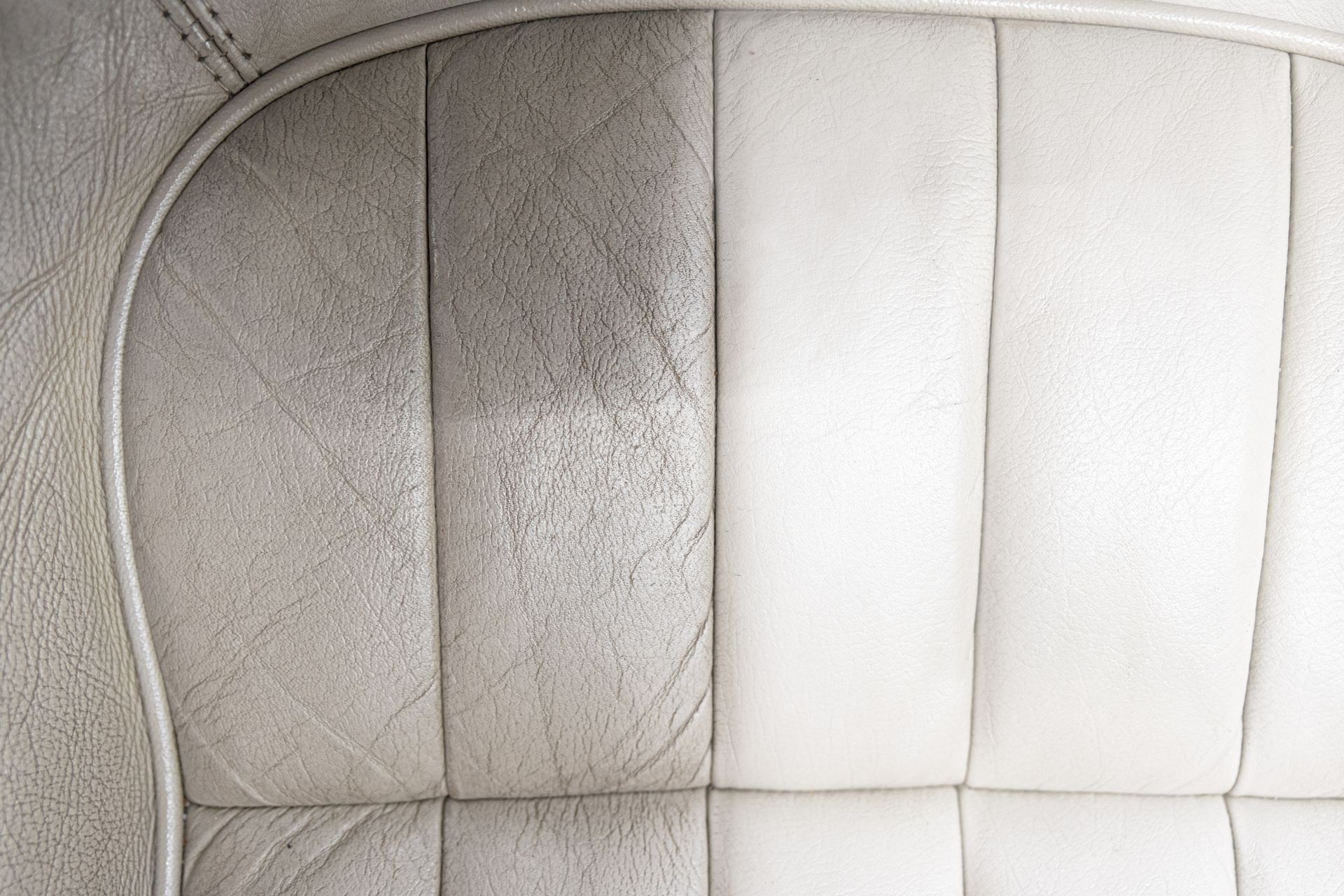 A side-by-side comparison of a leather car seat showing a dark, dirty section cleaned to a bright, off-white finish.