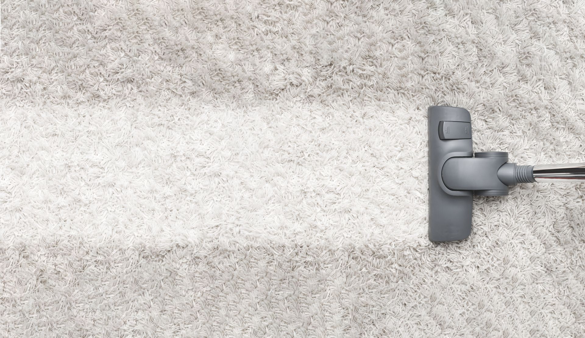 A gray vacuum cleaner head moving across a gray carpet, leaving a clean, bright path in its wake.