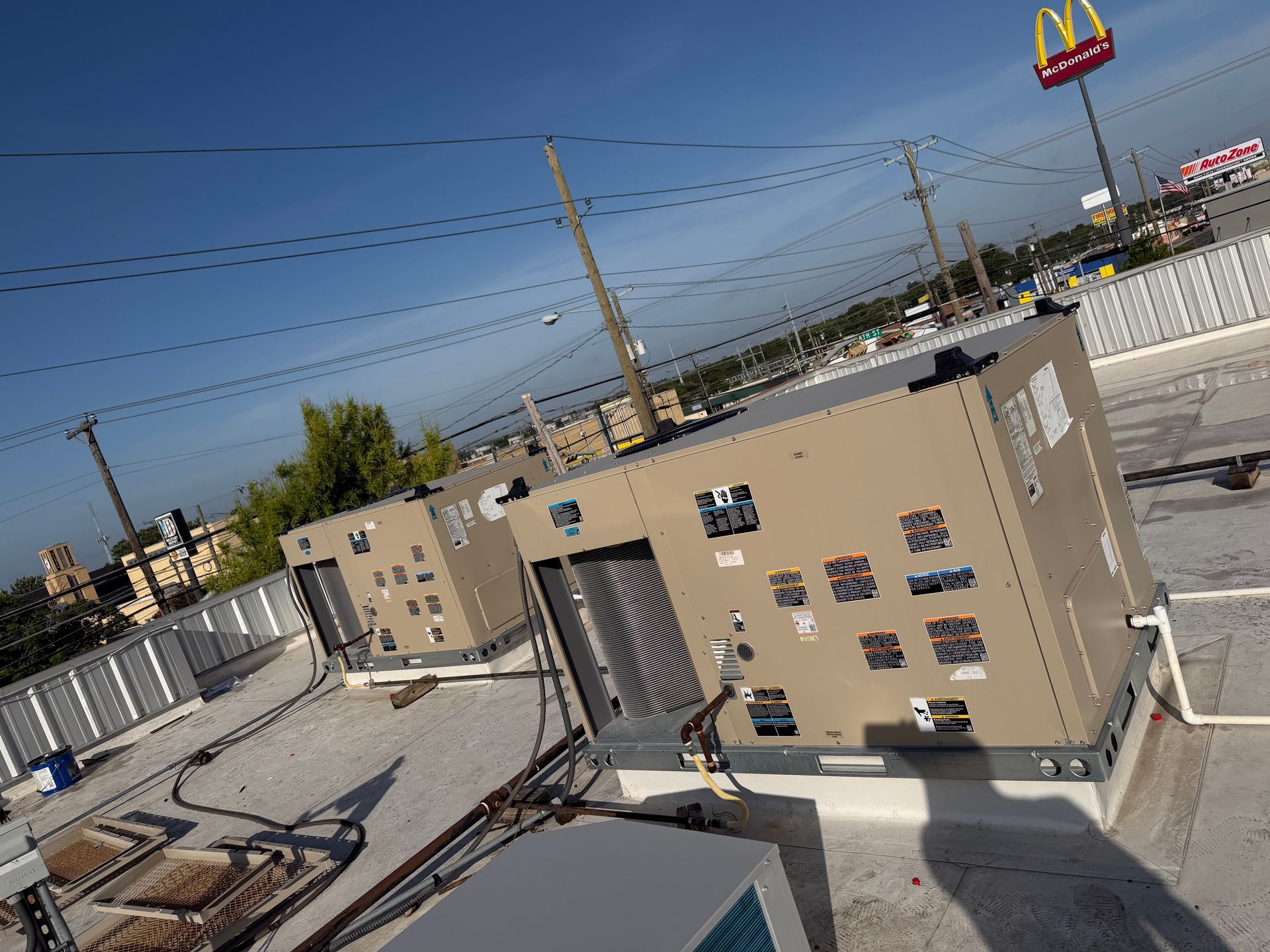 Rooftop with tan HVAC units and rooftop equipment under a clear sky, with McDonald’s arches in the distance