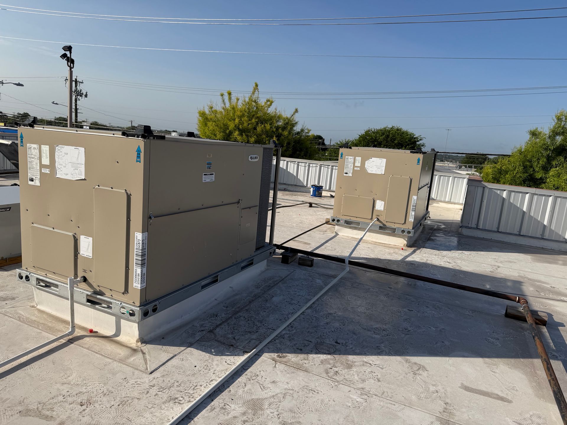 Rooftop HVAC units on a flat roof under a clear sky, with vents and pipes visible.