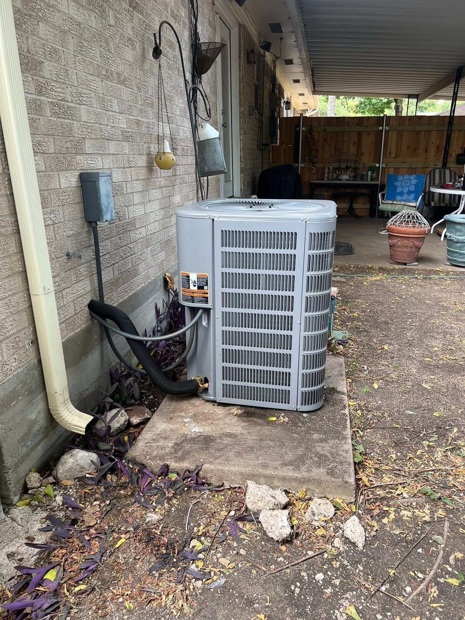 Outdoor air conditioner unit beside a stone house wall under a covered patio.