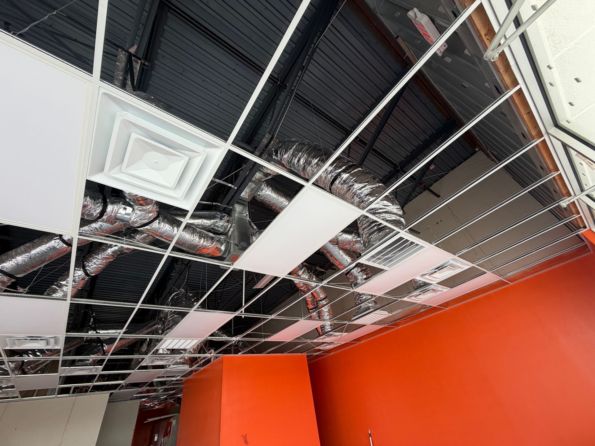 Damaged office ceiling with missing tiles, exposed wires, and red walls below