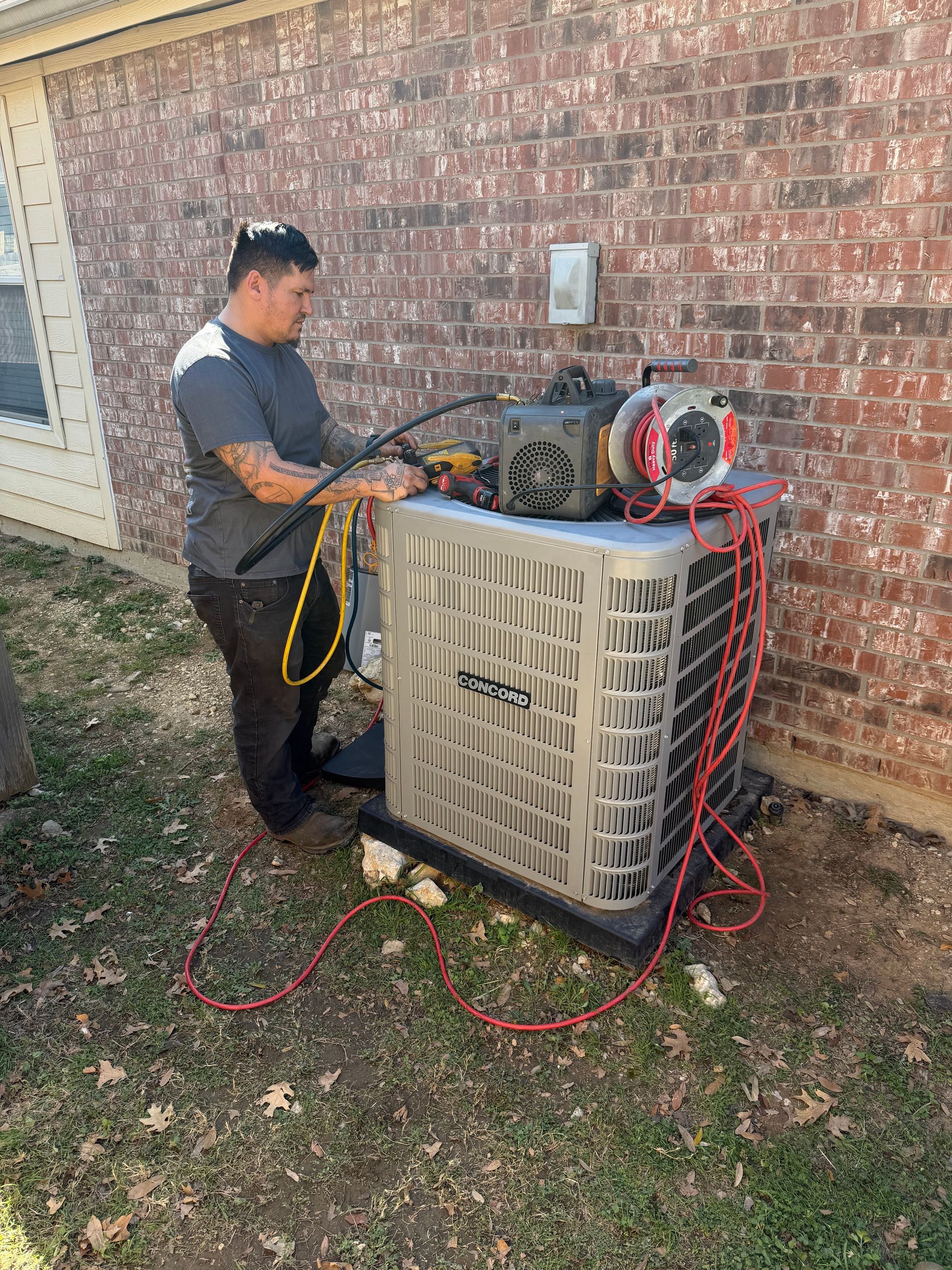 Technician working on an outdoor HVAC unit beside a brick wall, with tools and cables attached.