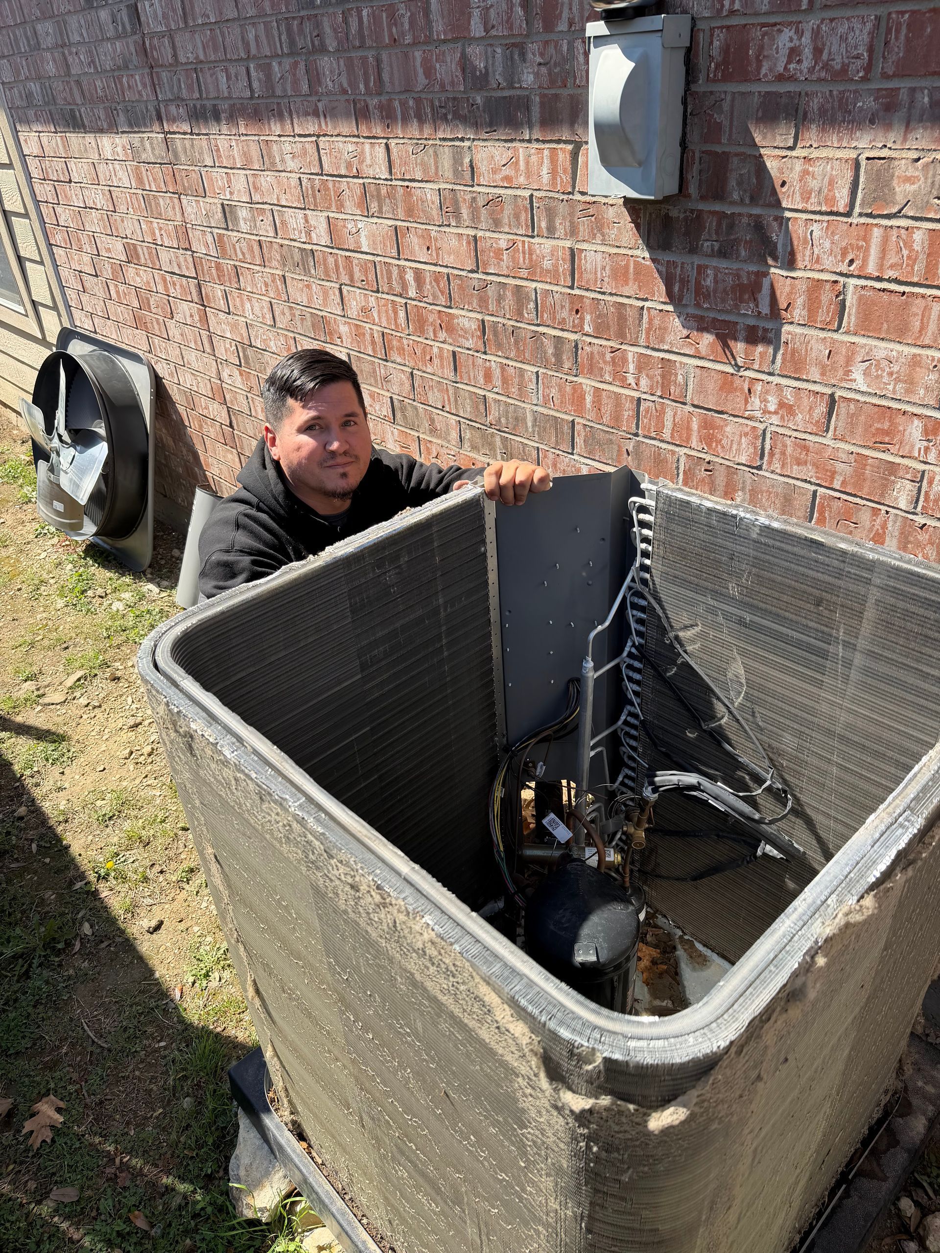Man crouching beside an open HVAC unit next to a brick building outdoors