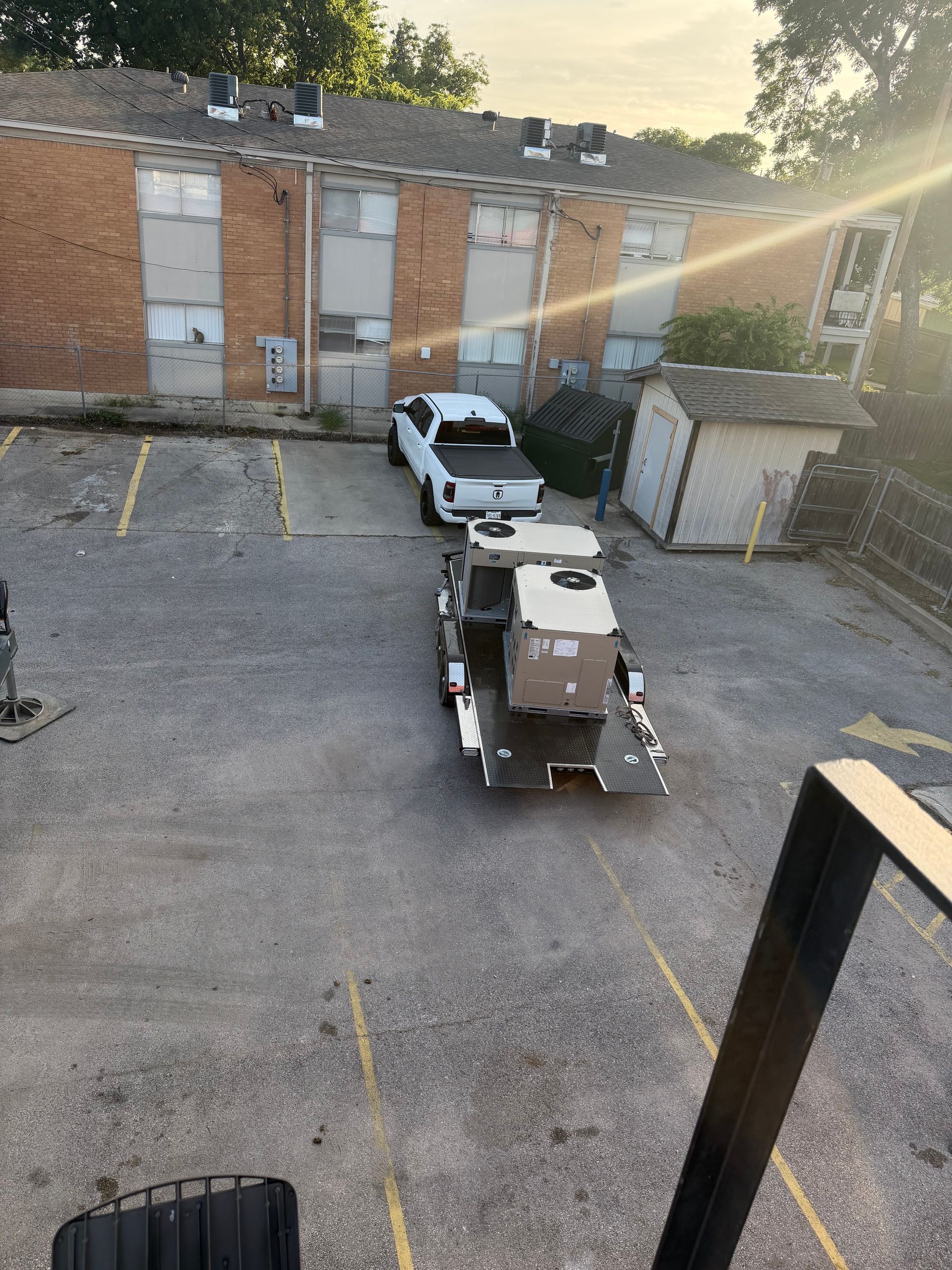 Parking lot with a white pickup and beige utility vehicle beside a brick building at sunset