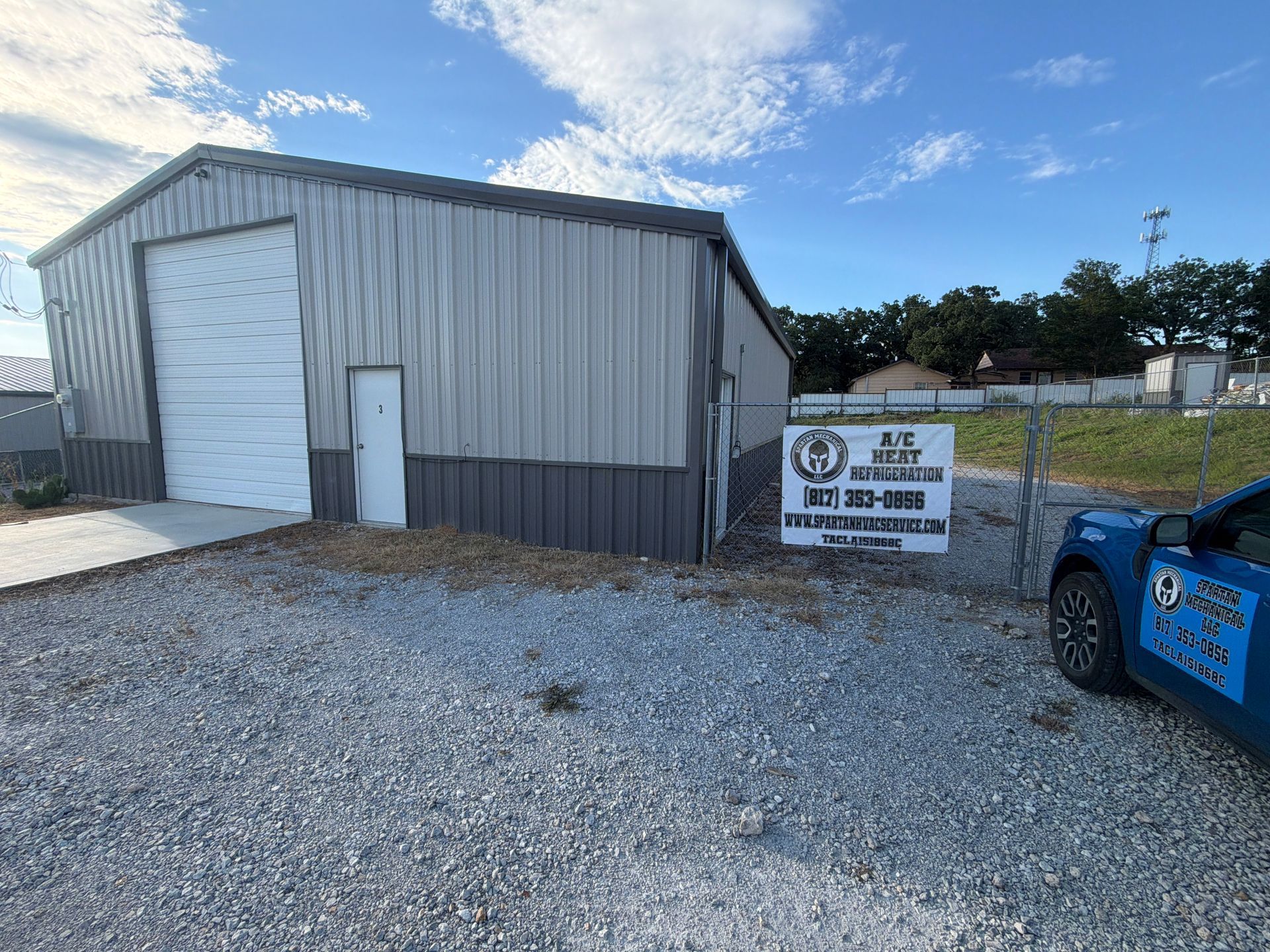 Gravel lot with gray metal garage, warning sign, and blue vehicle on the right.