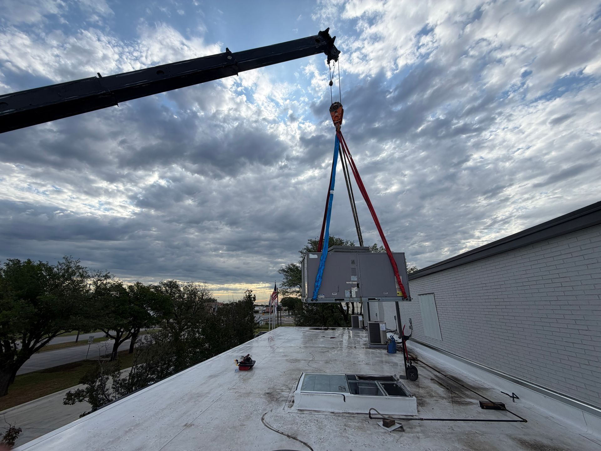 Crane lowering a red-and-blue suspended load onto a snowy rooftop beside a white building.