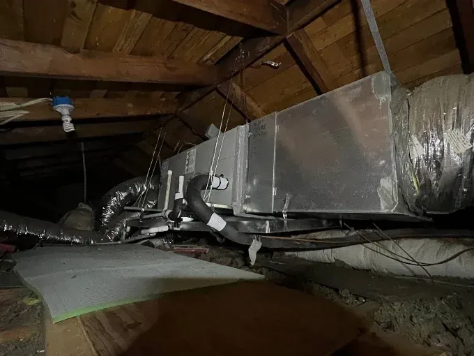 Attic with large silver HVAC ducts under exposed wooden rafters and insulation.