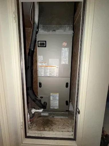 HVAC furnace in a narrow utility closet with exposed ductwork and dusty floor
