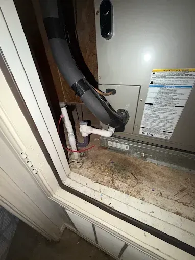HVAC unit with exposed drainage and insulation inside a utility closet, viewed through an open panel.