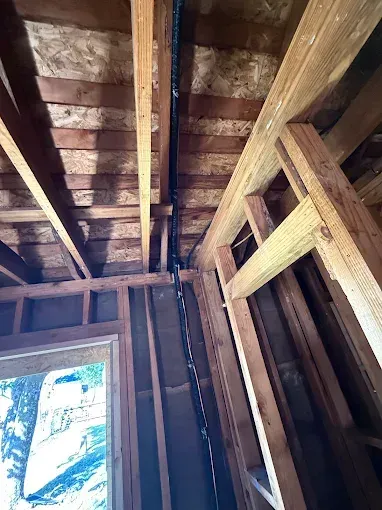 Interior framing of an unfinished room, showing exposed wooden beams and a small window with daylight.