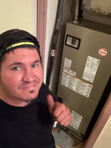 Man taking a selfie beside a furnace, giving a thumbs-up in a narrow hallway.