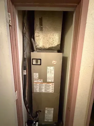 Air handler in a narrow utility closet with exposed ductwork and wiring