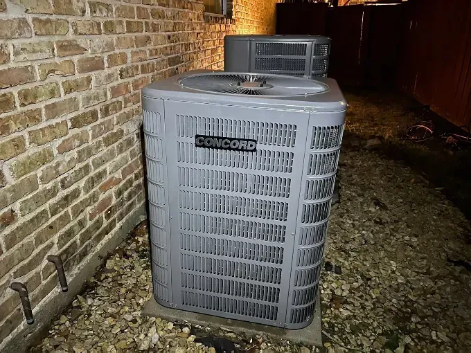 Outdoor air conditioner unit beside a brick wall at night