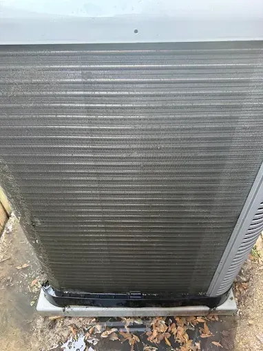 Close-up of a large gray HVAC unit with a bent base sitting on a concrete pad outdoors.