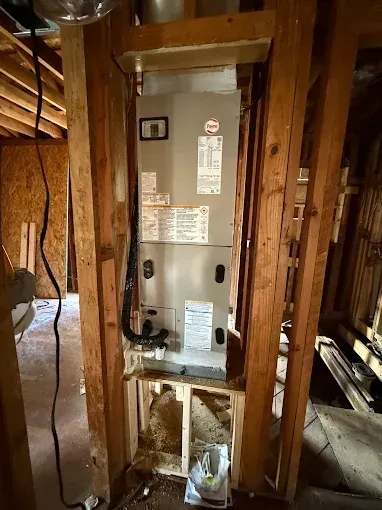 Water heater installed in an unfinished wooden utility closet with exposed pipes and wiring.