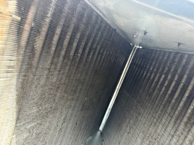 Inside a metal vent shaft with corrugated walls and a light fixture overhead