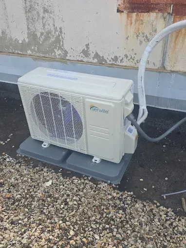 Outdoor HVAC unit on a concrete pad beside a wall, with a white hose attached.