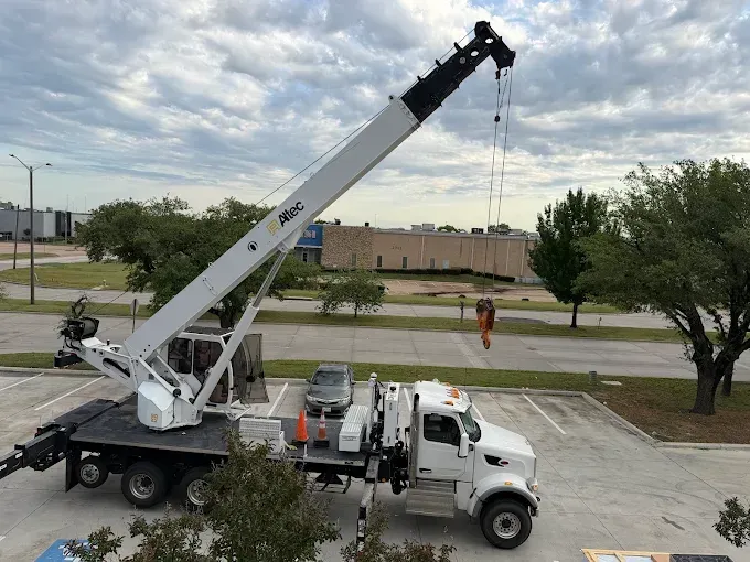 White utility crane truck with boom extended in a parking lot near trees and a building.