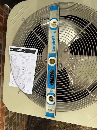 Wall-mounted beige industrial fan with a blue control panel and a paper notice clipped to the grille