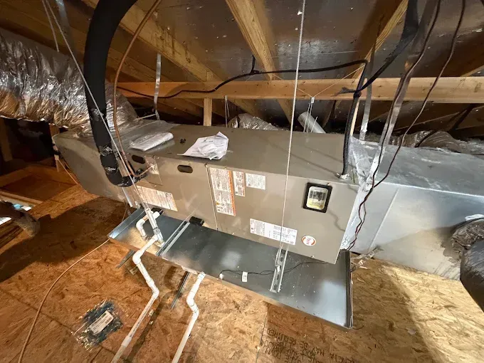Attic HVAC unit with exposed ductwork and wiring on wooden floor framing