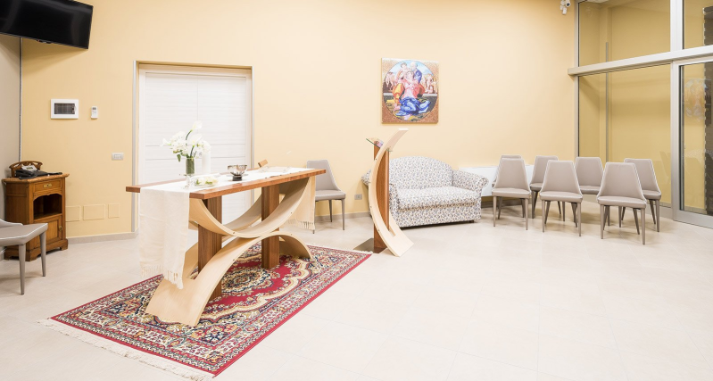 Bright waiting room with wooden benches, chairs, rug, and a small table near a door and window.