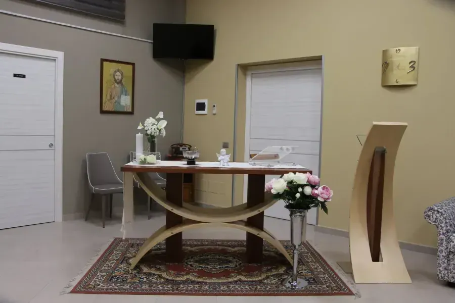 Waiting room with desk, flowers, chairs, wall clock, and closed doors on beige walls.