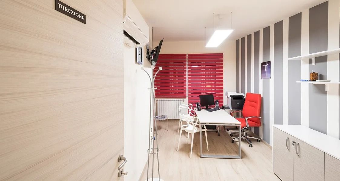 Bright office meeting room with white table, red chairs, blinds, and glass-partitioned walls.