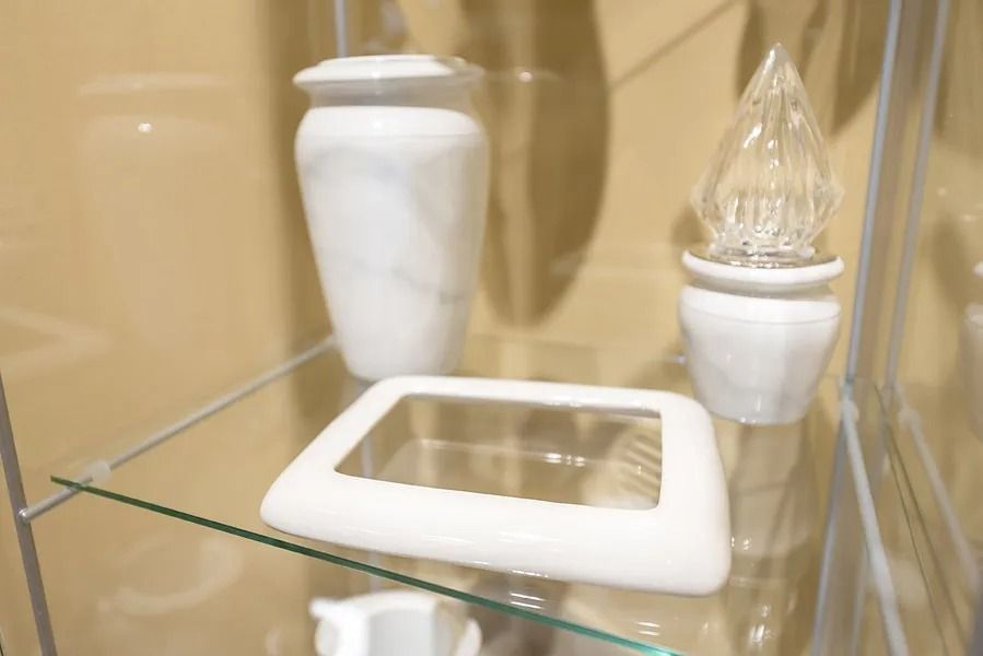 Glass shelf with two white decorative urns and a framed item in a display cabinet