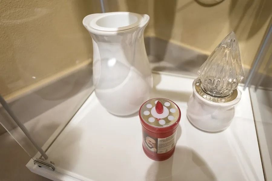 Bathroom shelf with a white vase, a red can, and a glass bottle on a white tray.