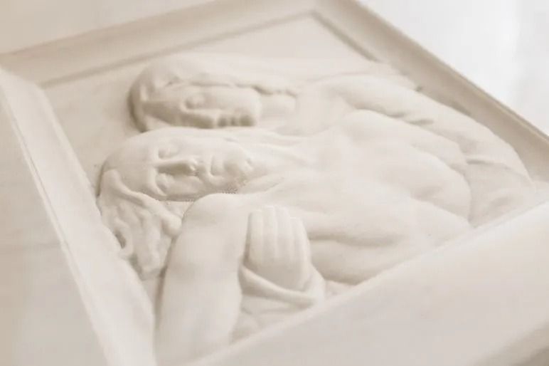 White relief sculpture of two sleeping figures in a shallow display box