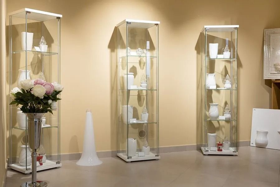 Display of glass cabinets with white ceramic pieces and a flower arrangement in a beige gallery room