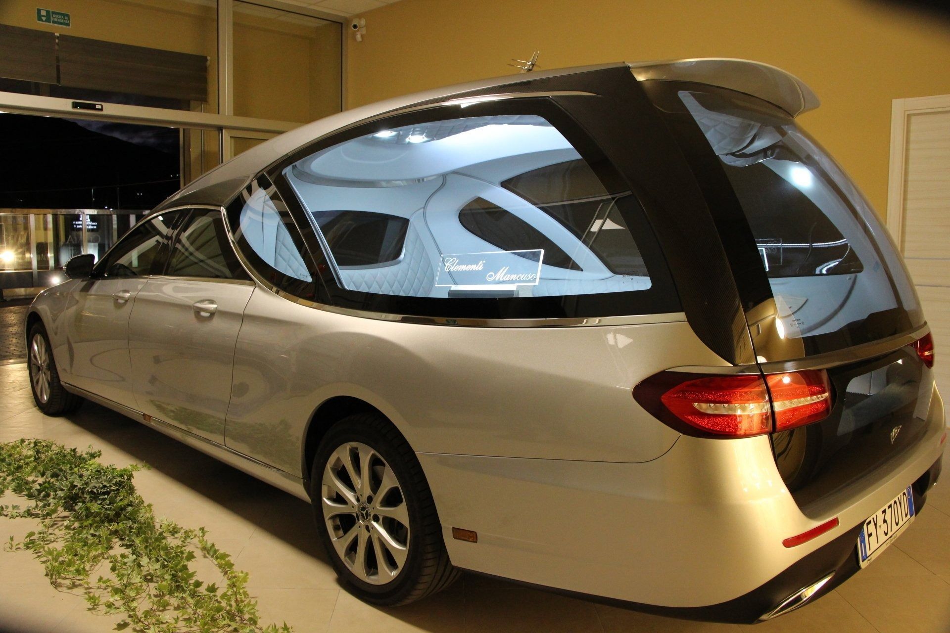 Silver minivan parked indoors in a garage, viewed from the rear side.