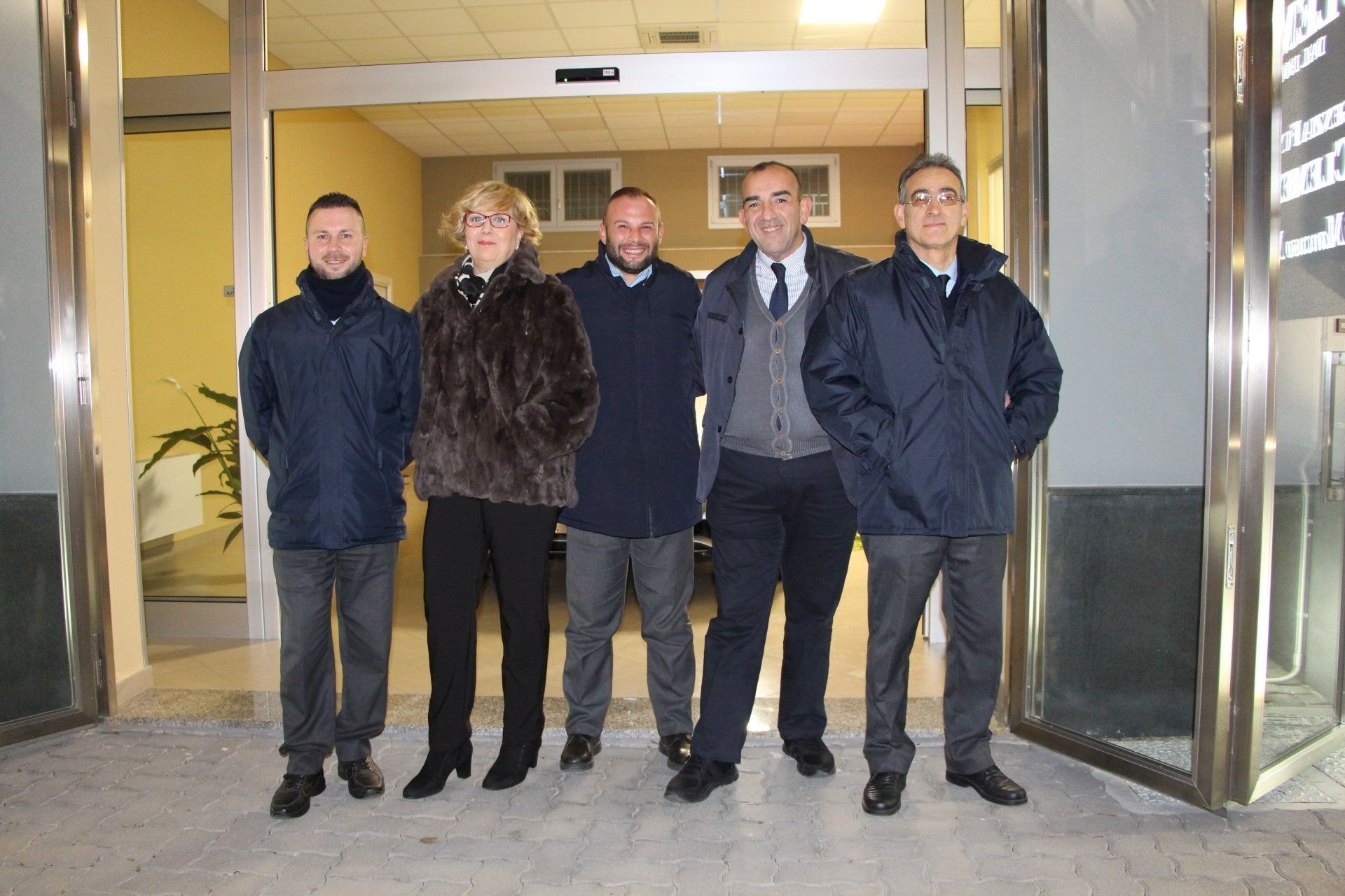 Four people standing at a building entrance, two in dark coats and one in a suit