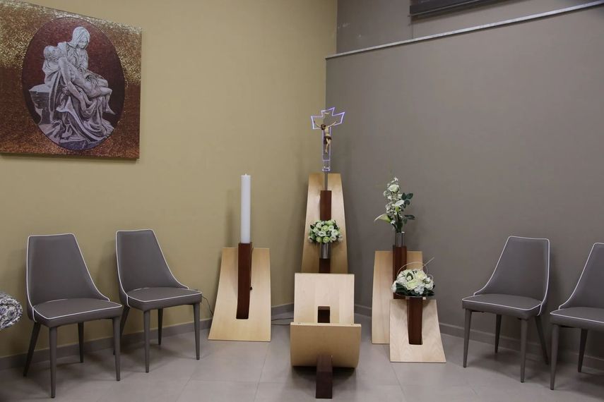Small memorial altar with chairs, flowers, candles, and a religious plaque in a quiet room