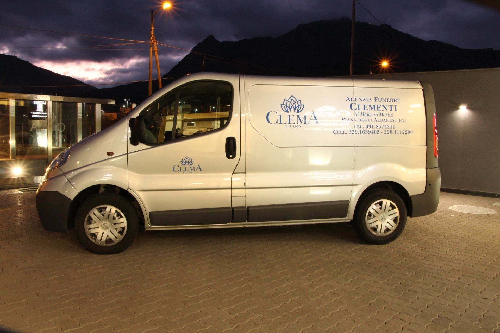 White cargo van with company logo parked at night under streetlights, with mountains in the background