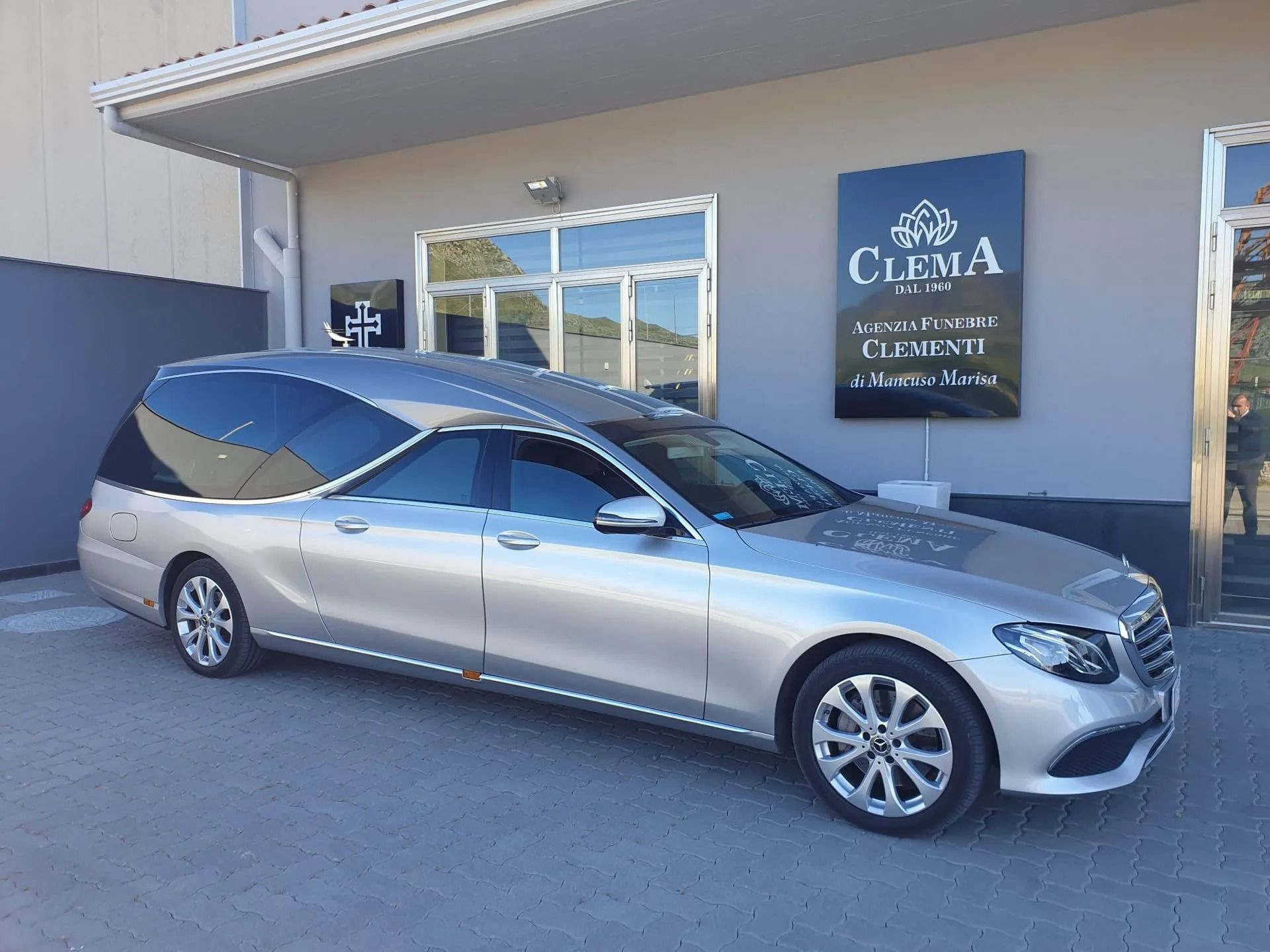 Silver station wagon parked outside a car dealership with a Clima sign on the building